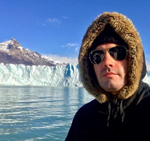 Close-up of man with sunglasses and warm clothing standing by lake during winter