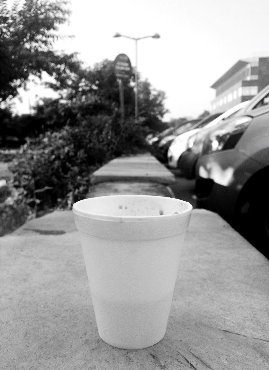 drink, architecture, built structure, building exterior, tree, sky, food and drink, day, coffee cup, outdoors, sunlight, close-up, refreshment, street light, table, focus on foreground, no people, street, white color, shadow