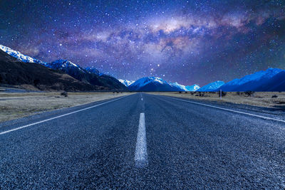 Road amidst snowcapped mountains against sky at night