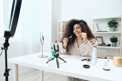 Happy woman gesturing while filming make-up tutorial on smart phone