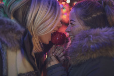 Female friends holding caramelized apple at night