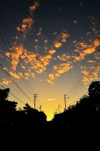 Silhouette electricity pylons against sky at sunset