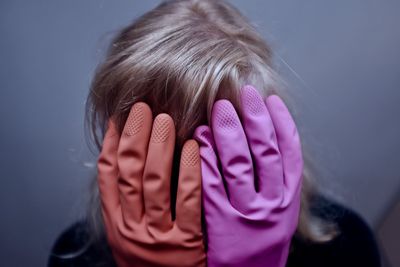 Woman wearing gloves covering face against wall
