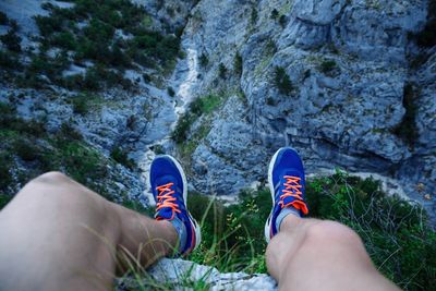 Low section of hiker sitting on cliff against rocky mountains