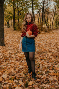 Portrait of smiling young woman standing by tree during autumn