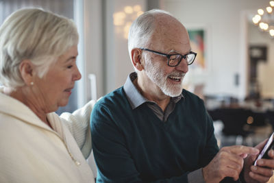 Smiling senior couple using smart phone while sitting in living room