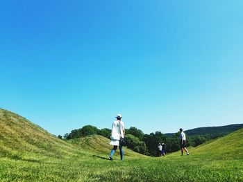 People walking on green landscape against clear blue sky