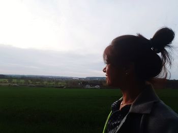 Portrait of young woman standing on field against sky