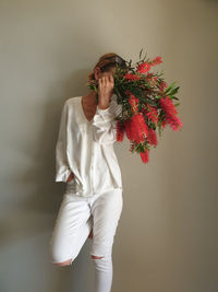 Portrait of woman standing against wall holding bouquet of bottlebrush flowers 