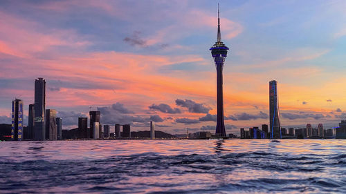 Communications tower in city against sky during sunset