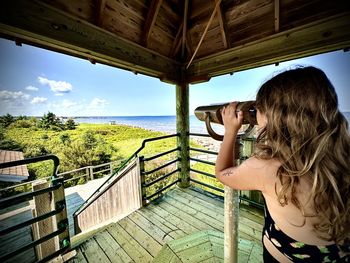 Rear view of woman photographing through binoculars against sky