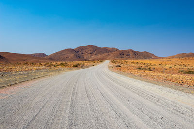 Road amidst desert against clear blue sky