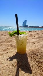 Disposable cup with drink at sandy beach against w barcelona