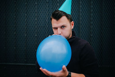 Portrait of man blowing balloon against metal grate