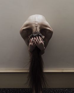 Depressed naked woman bending against wall