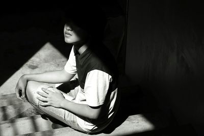 Young person looking away while sitting on floor int the dark with a beam of light