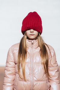 Girl in wall clothing covering eyes through knit hat against white wall