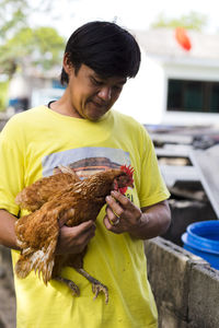 Farmer holding hen while standing outdoors