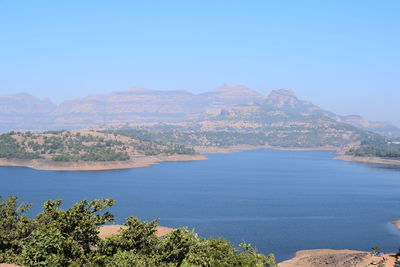 Scenic view of sea and mountains against clear blue sky