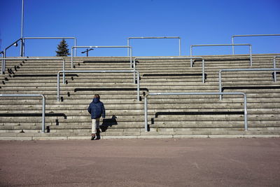 Rear view of boy on staircase against clear sky