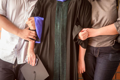 Midsection of people standing arm in arm against brick wall