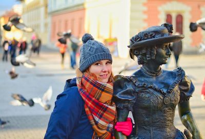 Portrait of woman standing by metallic statue in city