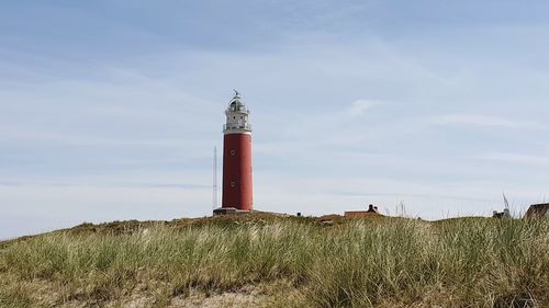 Lighthouse on field by building against sky