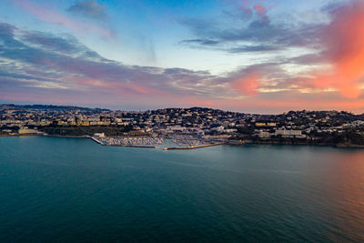 Scenic view of sea by buildings against sky during sunset