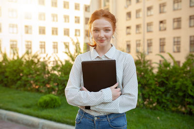 Woman holding book while standing in campus