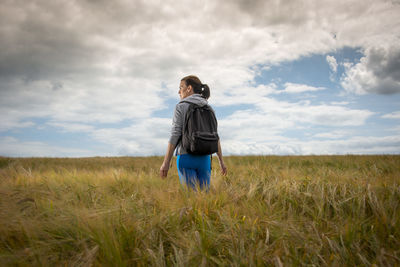 Woman with a backpack walking through a field, enjoying the countryside.