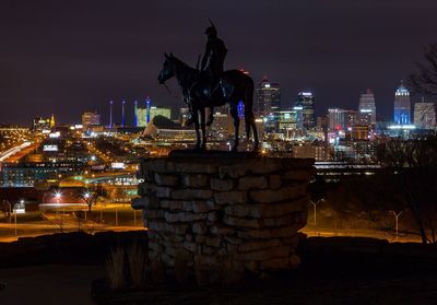 Statue against illuminated city at night