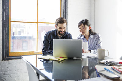 Smiling business people using laptop at creative office