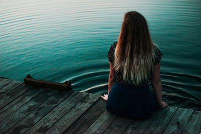 Rear view of teenage girl sitting on pier over lake