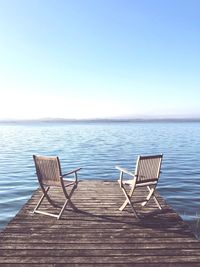 Empty chair on sea against clear sky