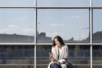 Woman looking at camera while sitting on window