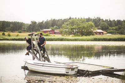 Boyfriend and girlfriend sitting on diving platform at jetty by lake during weekend