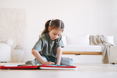 Preschool little girl is sitting on the floor and drawing at bright room at the home