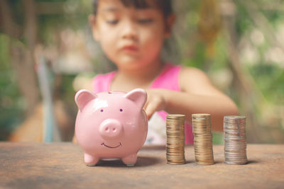 Close-up of a girl with piggy bank and stack of coins