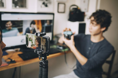 Girl filming friend on mobile phone using camera while sitting at home