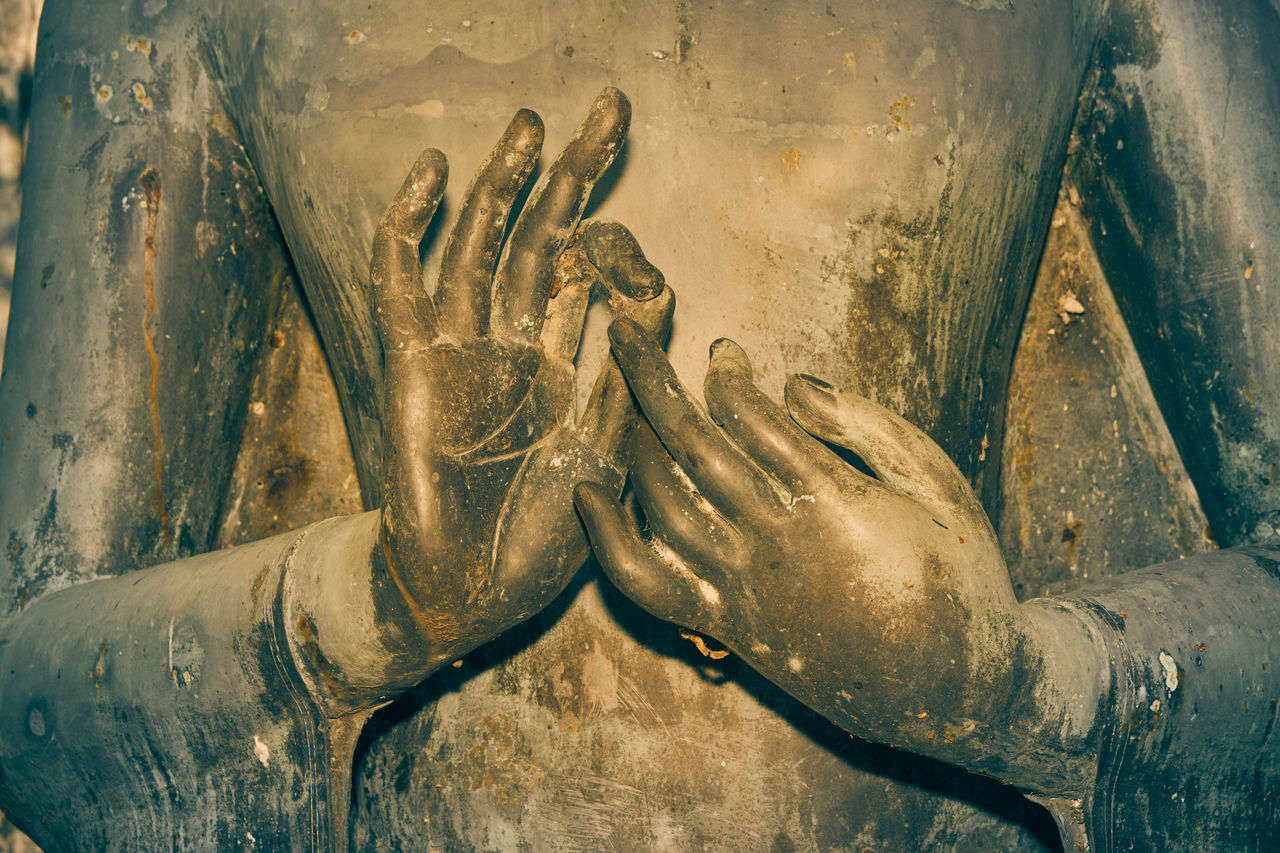 CLOSE-UP OF HUMAN HAND AGAINST STATUE