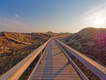 Boardwalk amidst mountains against sky during sunset