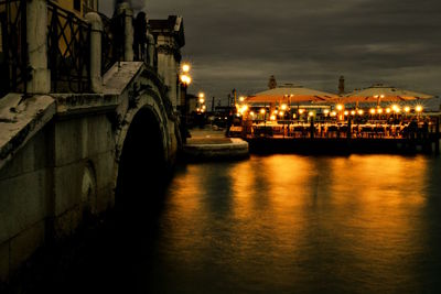 Illuminated bridge over river against sky at night