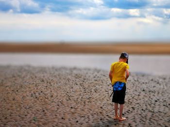 Rear view of boy standing on sand at beach