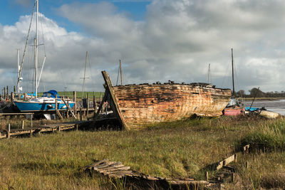 Abandoned boats moored on grass against sky
