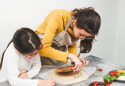 Caucasian girls sisters together cuts dough on a wooden plate with a metal scabbard .