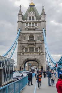 Group of people walking on bridge against cloudy sky