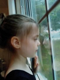 Close-up portrait of girl looking through glass window