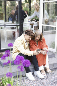 Full length of young man sharing smart phone with mother while sitting on steps