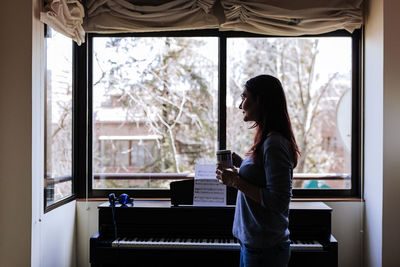 Woman looking through window at home