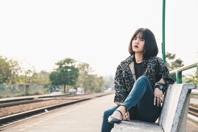 Full length portrait of woman sitting on bench at railroad station platform